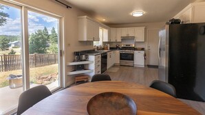 A modern kitchen with white cabinets, a black refrigerator, and a dining area with a wooden table and chairs.