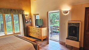 Ein Schlafzimmer mit einem großen Bett, einer Holzkommode, einem Fernseher und einem Kamin. Eine Glastür öffnet sich zu einer Außenpatio.