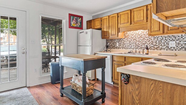 A kitchen with wooden cabinets, a white refrigerator, a tiled backsplash, and a small dining table with chairs. - Five Points Dawg Crib On Campus (Athens)