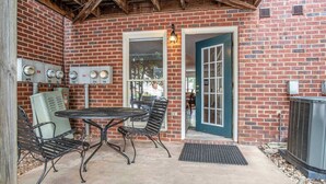 An outdoor patio with a brick wall, a table with chairs, a door, and an air conditioning unit. - Five Points Dawg Crib On Campus (Athens)