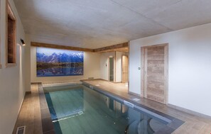 A modern indoor swimming pool with a large mural of mountains and a lake.