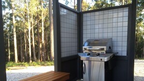 An outdoor grill with a wooden table in a wooded area. - High Peaks Cottages (Fumina South)