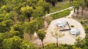 An aerial view of a property with a central building surrounded by a dirt driveway and a few trees. - High Peaks Cottages (Fumina South)