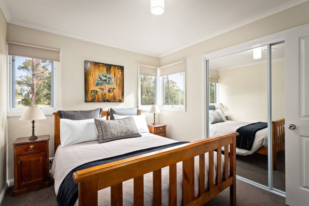 Une chambre à coucher avec un lit en bois, deux tables de chevet, une commode, un grand miroir et un tableau accroché au mur.