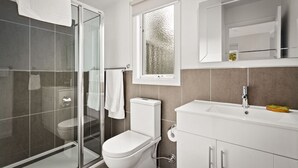 A modern bathroom with a glass-enclosed shower, a toilet, and a sink with a mirror above it. - High Peaks Cottages (Fumina South)