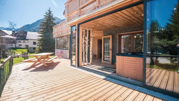A wooden deck with a hot tub, a wooden table, and chairs. - Chalet, wifi, 80m from ski slopes, terrace, parking, tv, ski locker, 300m², Les 2 Alpes (Les Deux Alpes)
