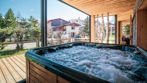 A hot tub with a wooden deck and large windows overlooking a residential area. - Chalet, wifi, 80m from ski slopes, terrace, parking, tv, ski locker, 300m², Les 2 Alpes (Les Deux Alpes)