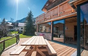 A wooden deck with a picnic table, a glass-enclosed room with a view of the mountains, and a wooden fence. - Chalet, wifi, resort center, terrace, parking, tv, ski locker, 300m², Les 2 Alpes (Les Deux Alpes)