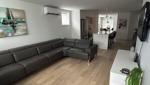 Een moderne woonkamer met een hoekbank, een eethoek met een witte tafel en stoelen, en een keuken op de achtergrond.