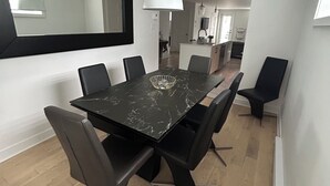 Een moderne eetruimte met een zwart marmeren tafel, zwarte stoelen, een grote spiegel en een witte hanglamp.
