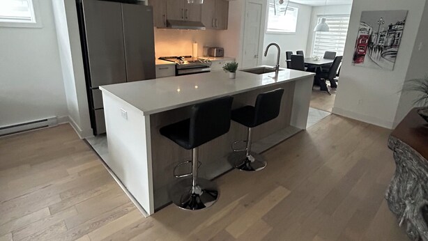 Een moderne keuken met een centraal eiland, roestvrijstalen apparatuur en zwarte barkrukken.