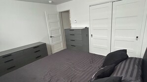 Een slaapkamer met een bed, twee kledingkasten, een dressoir en een deur.