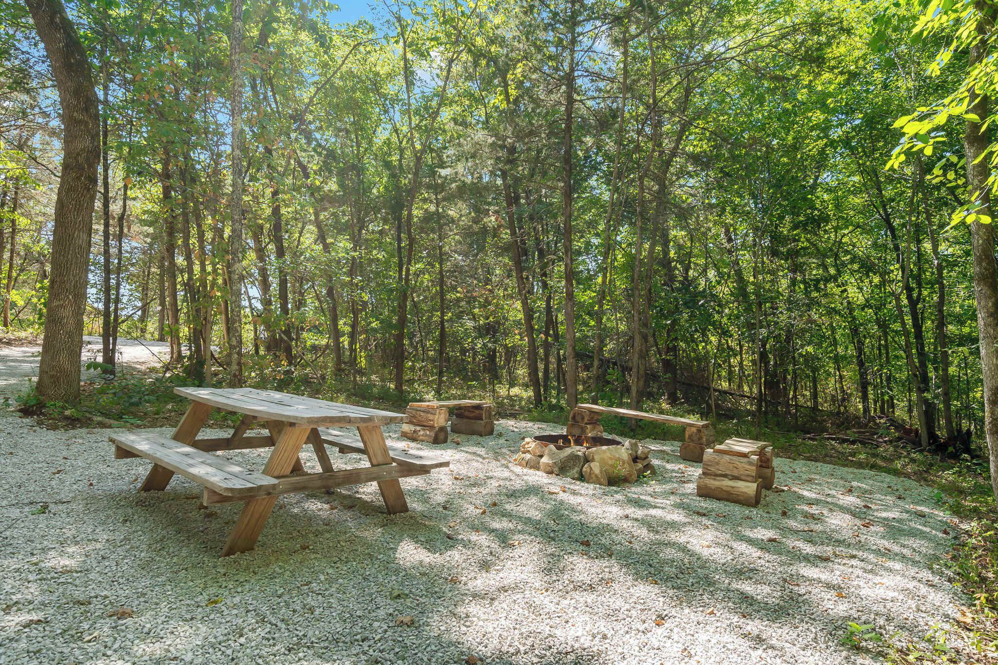A forested campsite with picnic tables and a fire pit.