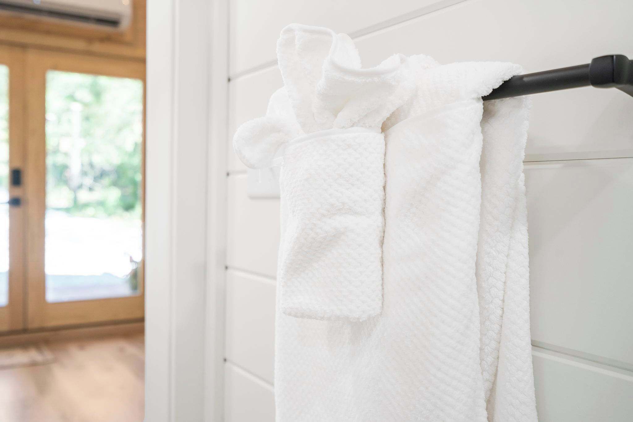 Una toalla blanca colgada en un toallero negro en un baño con paredes de azulejos blancos y una puerta de madera.