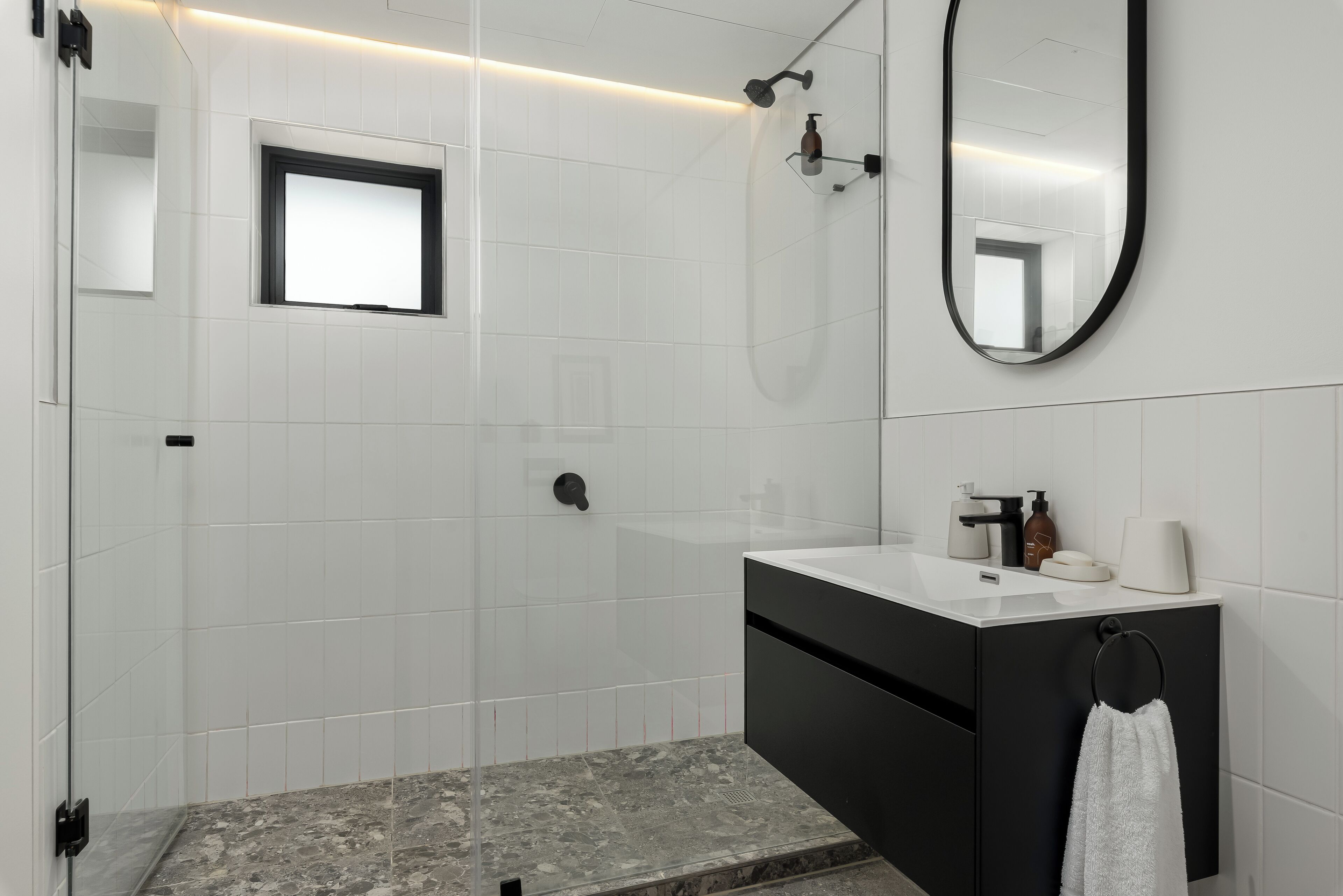 A modern bathroom with white tiles, a black vanity, a mirror, and a shower.