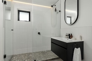 A modern bathroom with white tiles, a black vanity, a mirror, and a shower. - 529 Station House (Cape Town)