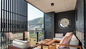A balcony with a wooden table and two sofas, a round mirror, and a view of buildings and hills. - 529 Station House (Cape Town)