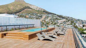 A rooftop pool area with lounge chairs and a view of a hill with a distinctive peak. - 529 Station House (Cape Town)