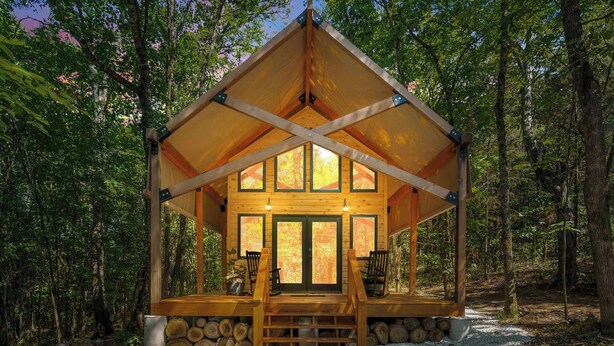 Una cabaña de madera con porche cubierto, ventanas amplias y cimientos de piedra.