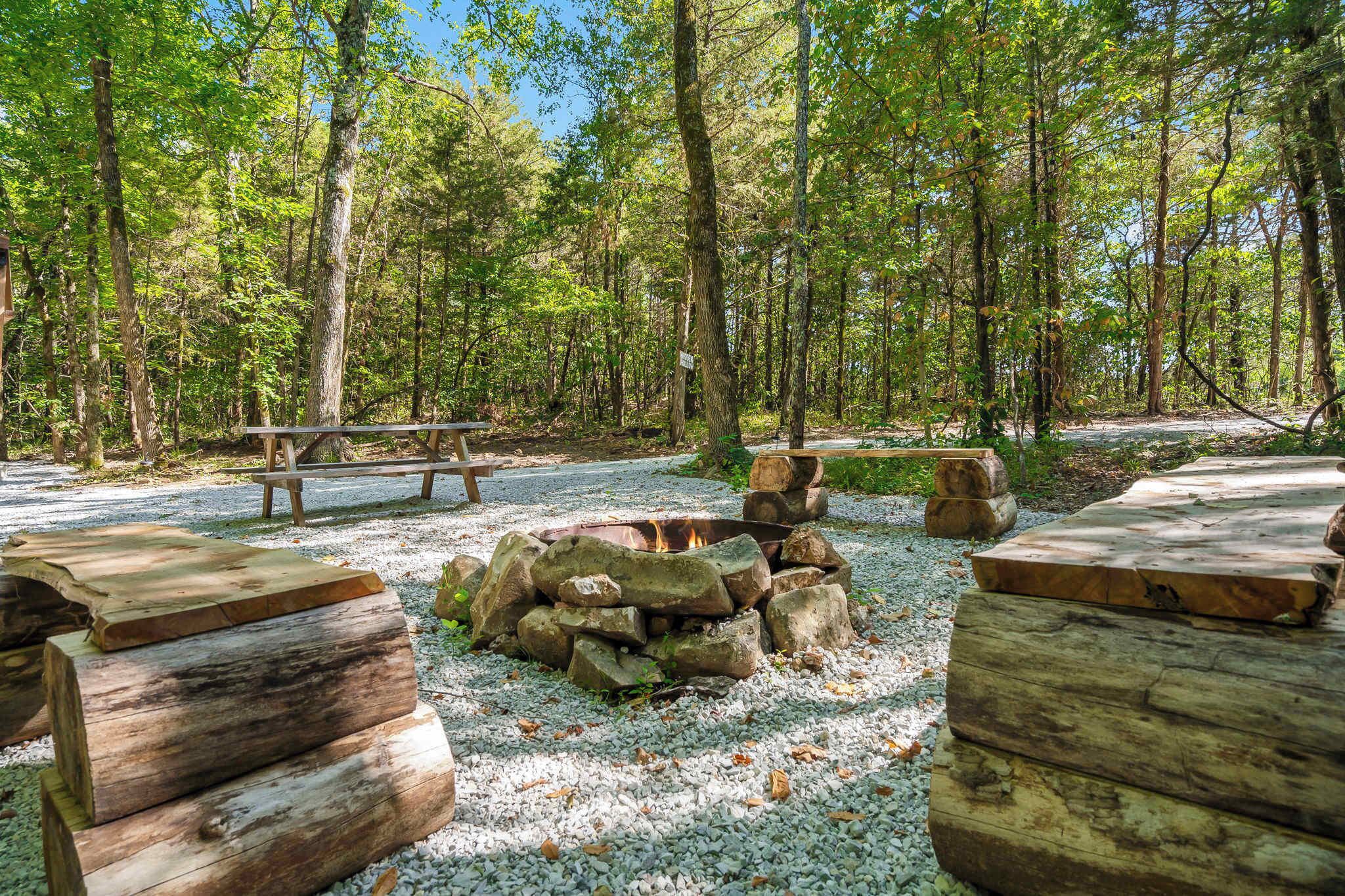 Un terrain de camping équipé d’un foyer, d’une table de pique-nique et de bancs en bois.