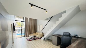 Una sala moderna con una escalera, un sofá, una mesa de centro y un escritorio con una silla.