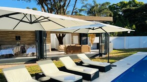 Un área junto a la piscina con sillas de descanso, sombrillas y una zona de comedor.