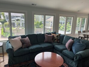 A modern living room with a sectional sofa, a round coffee table, and large windows offering a view of the neighborhood.