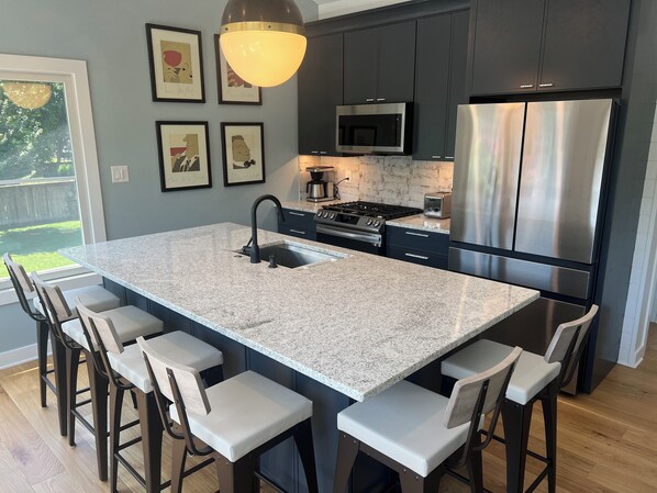 A modern kitchen with a large island, bar stools, stainless steel appliances, and framed artwork on the wall.