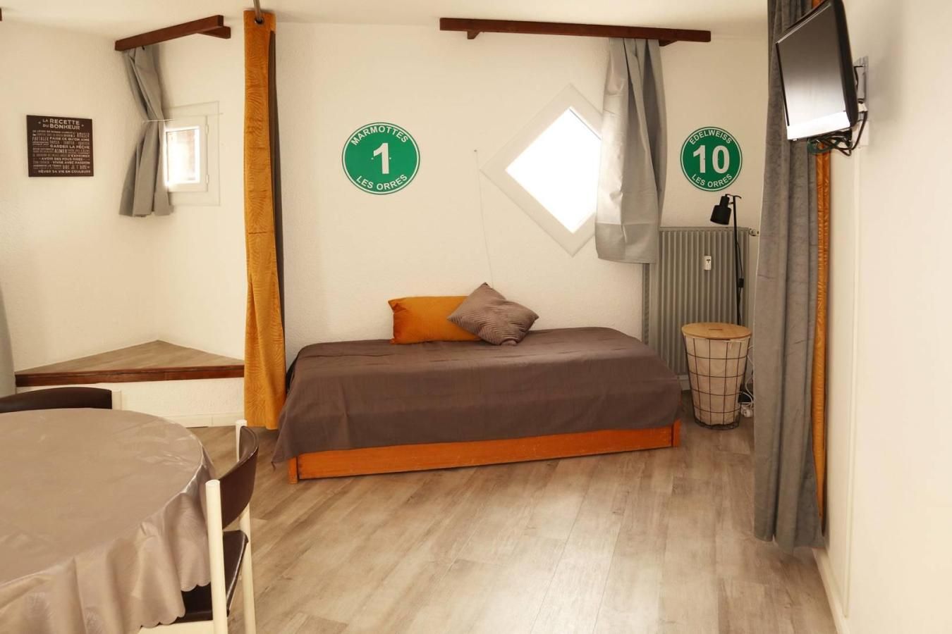 Ein Schlafzimmer mit einem Bett, einem kleinen Tisch, einem Stuhl, einem Fenster und einem an der Wand befestigten Fernseher.