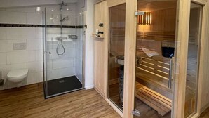 Un baño moderno con cabina de ducha de vidrio, sauna de madera y váter blanco.