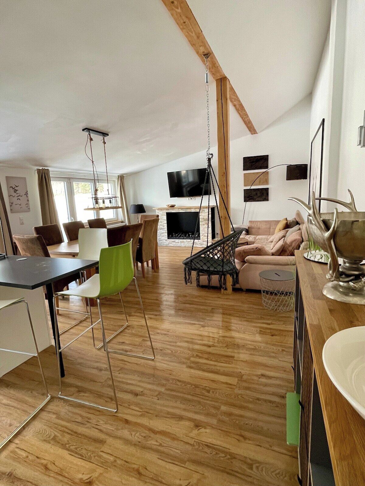 Un vaste espace de vie comprenant une table à manger, des chaises, un canapé, un téléviseur et un fauteuil suspendu.