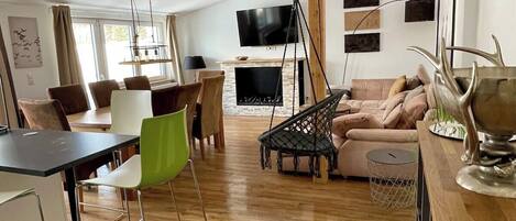 Un vaste espace de vie comprenant une table à manger, des chaises, un canapé, un téléviseur et un fauteuil suspendu.