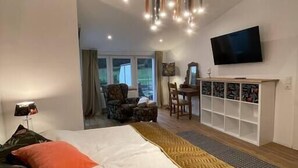 Una habitación de hotel moderna con una cama grande, un televisor montado en la pared y una zona de estar con chimenea.