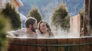 A couple in a hot tub with steam rising, surrounded by trees and a wooden fence. - Chalet, wifi, swimming pool, terrace, parking, tv, 62m², Les Orres (Les Orres)