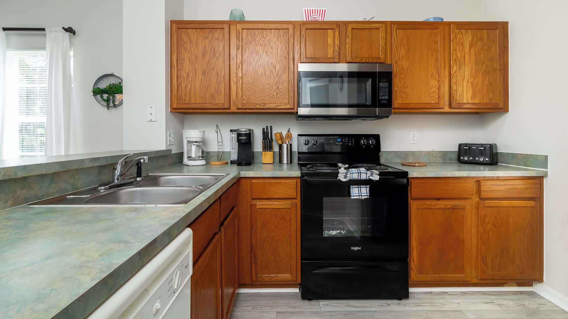 A modern kitchen with wooden cabinets, a stainless steel microwave, a black stove, and a dishwasher.
