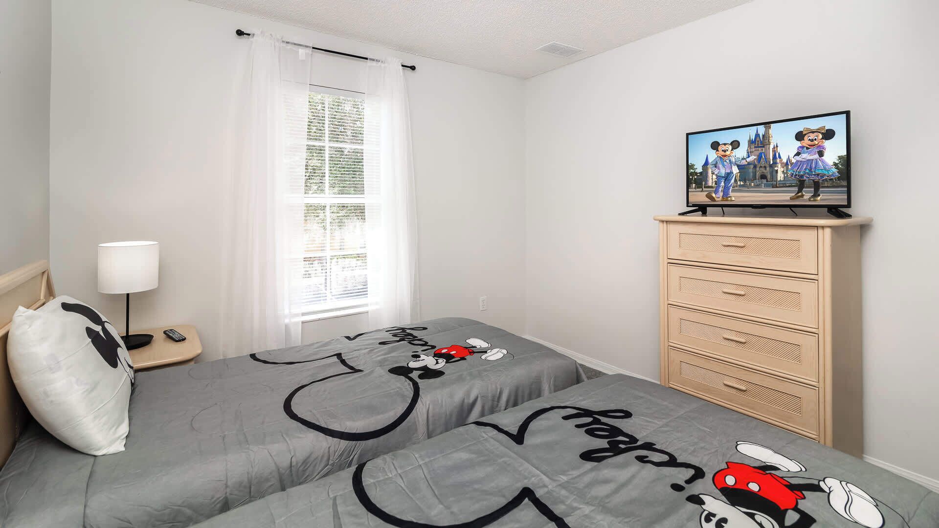 A bedroom with two beds, a TV on a dresser, a lamp, and a window with curtains.