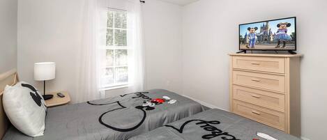 A bedroom with two beds, a TV on a dresser, a lamp, and a window with curtains.