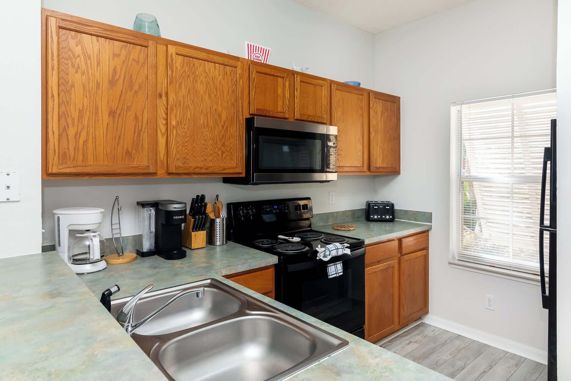 A kitchen with wooden cabinets, a stainless steel sink, a black microwave, a stove, and a toaster.