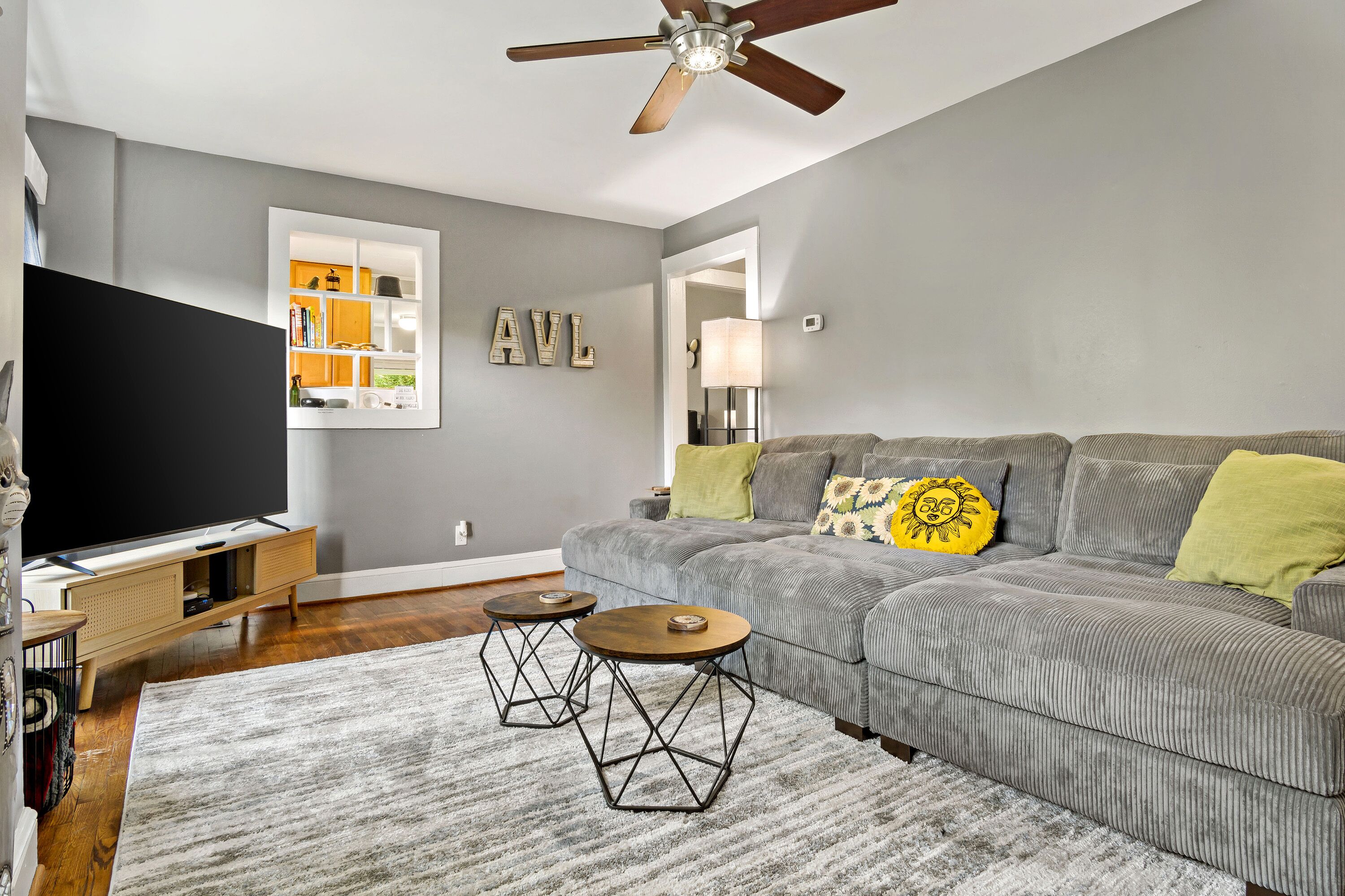 A living room with a grey sofa, two black metal tables, a TV, and a ceiling fan.