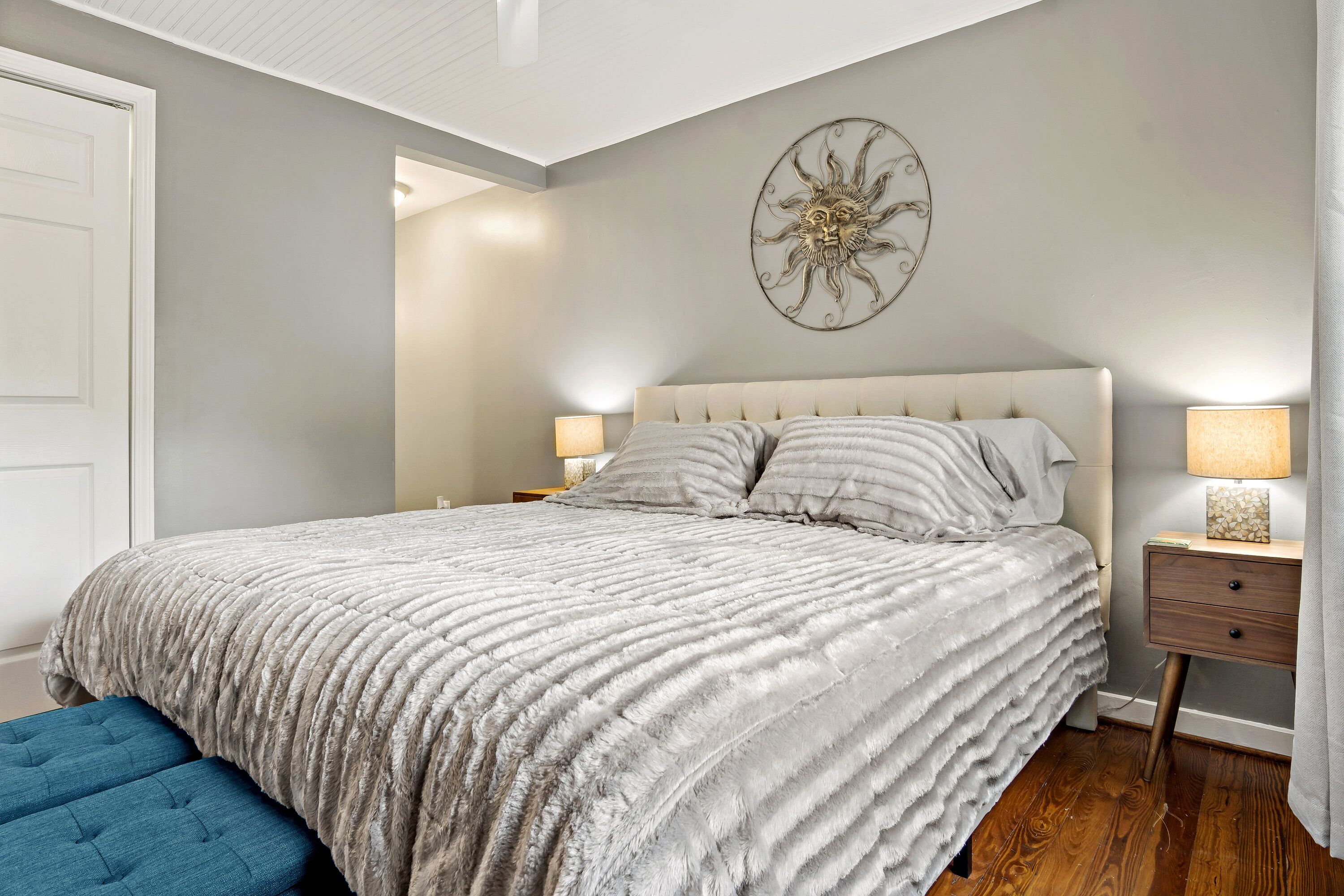 A bedroom with a large bed, two bedside tables, a wall-mounted decorative piece, and a blue bench.