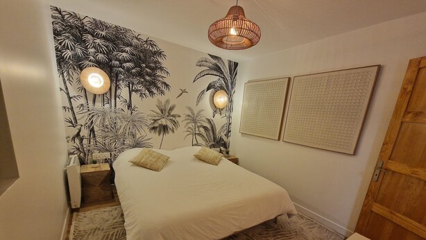 A bedroom with a bed, two wall-mounted lamps, a tropical mural, and two puzzle wall art pieces.