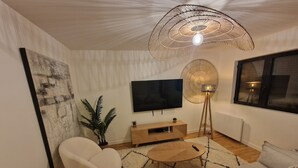 A modern living room with a sofa, armchair, TV, floor lamp, and a large painting on the wall.