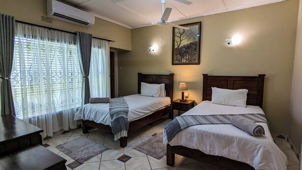 Une chambre d’hôtel avec deux lits, un ventilateur de plafond, un climatiseur, un tableau et une fenêtre avec des rideaux.