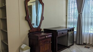 Une pièce comprenant une commode en bois, un miroir, un placard, une poubelle et une fenêtre avec des rideaux.