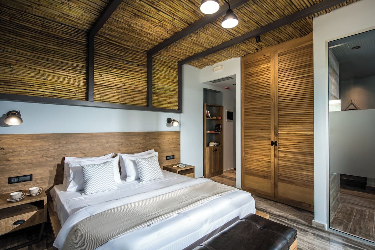 Un dormitorio moderno con cabecera de madera, una cama grande con ropa blanca, una mesita de noche con lámpara y un armario con espejo.