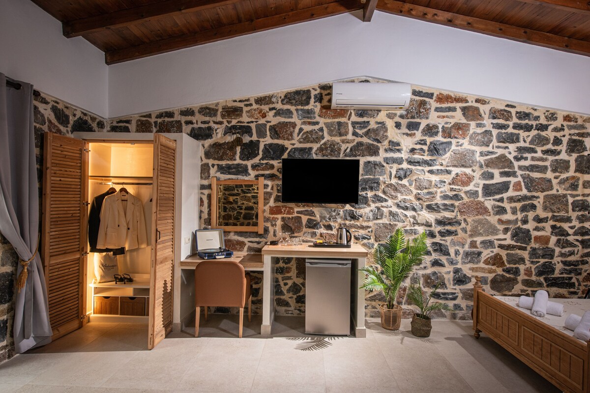 Un dormitorio con pared de piedra, una cama, un escritorio con computadora y un televisor montado en la pared.