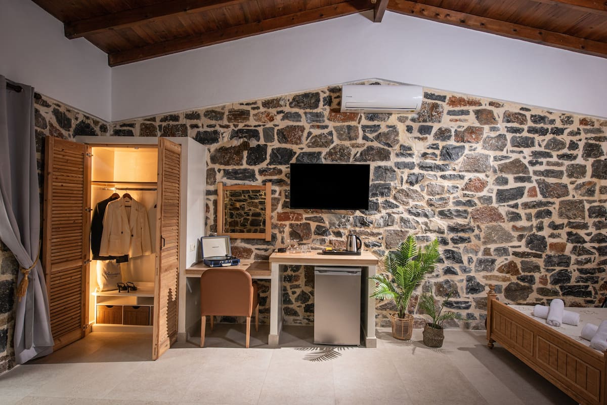 Un dormitorio con pared de piedra, una cama, un escritorio con computadora y un televisor montado en la pared.