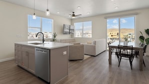A modern kitchen with a central island, a dining area with a table and chairs, and a living room with a sofa. - Boots at Kat's: Desert Color Lagoon + Beaches (St. George)