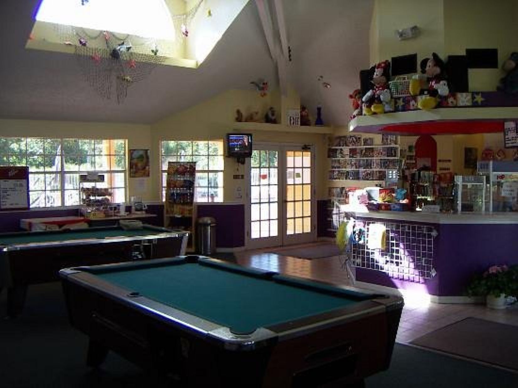 Ein Billardtisch in einem Raum mit hoher Decke, eine Bar mit Regalen und ein großes Fenster für natürliches Licht.