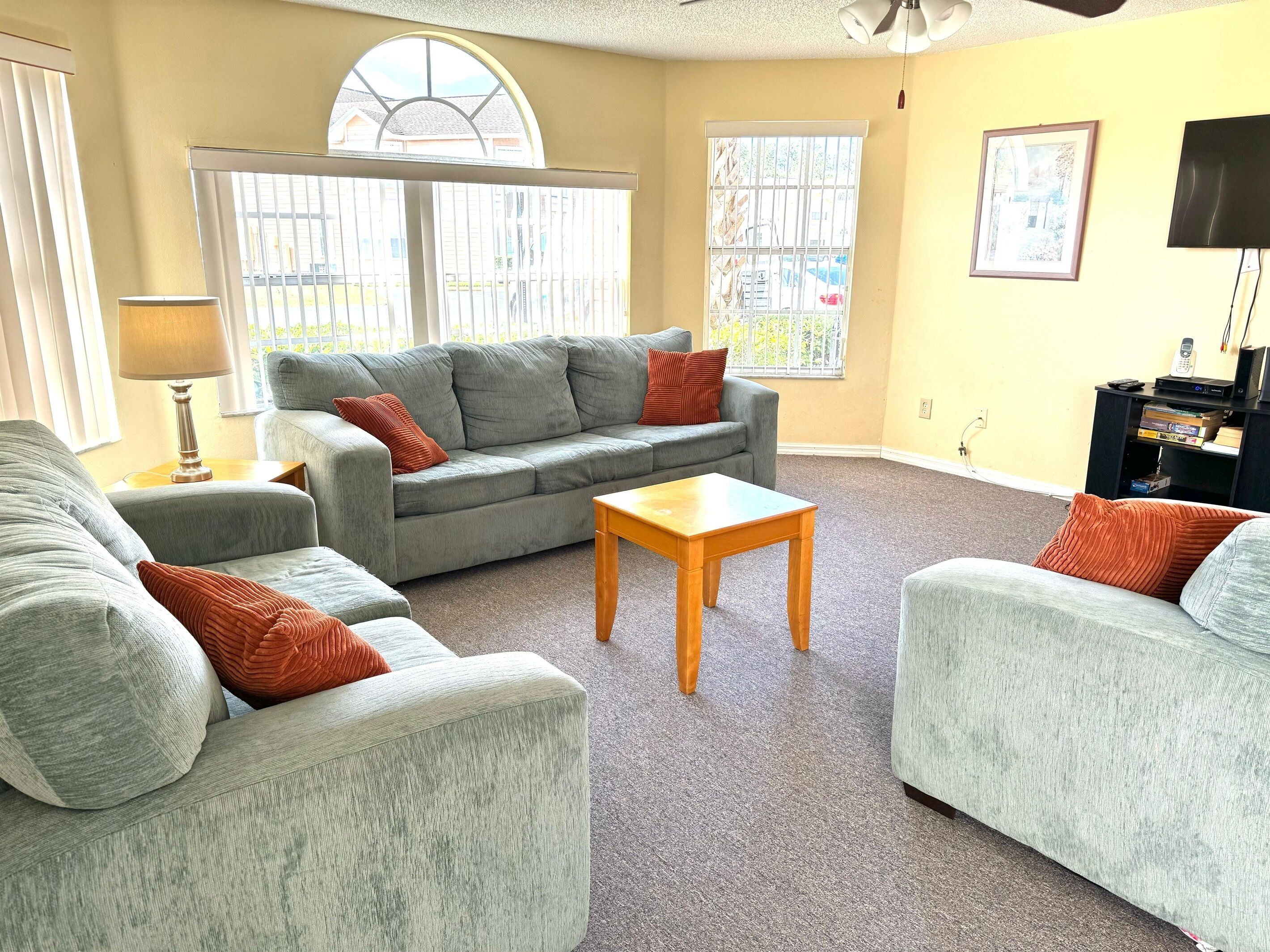 A living room with a grey sofa set, a wooden coffee table, and a TV stand with electronic devices.